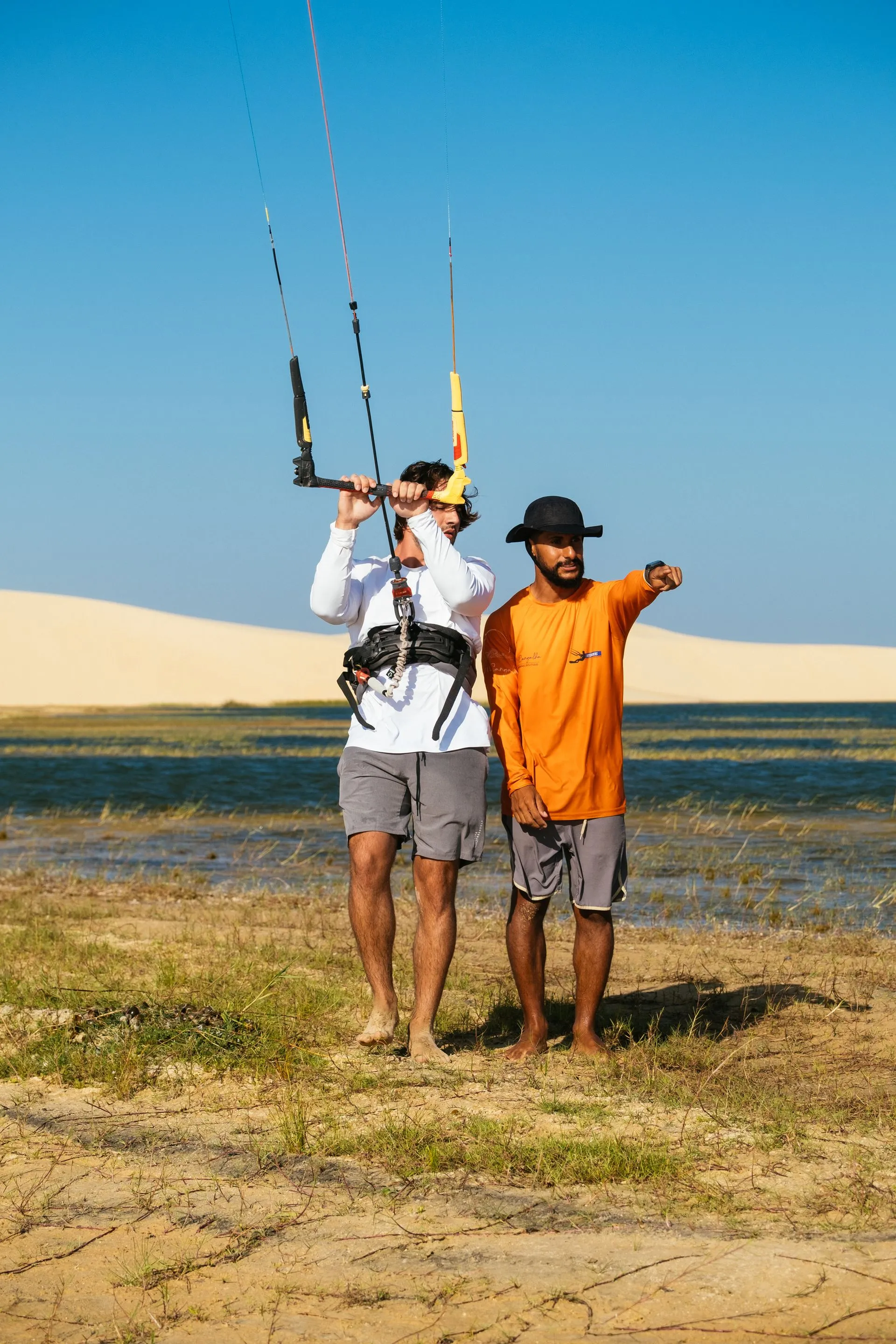 Aluno controla a barra do kite enquanto o instrutor aponta a direção do vento