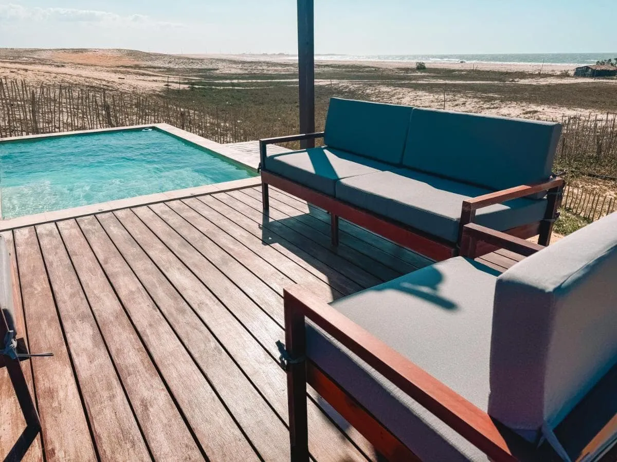 Deck de madeira com sofás de encosto baixo ao lado da piscina, voltados para o mar