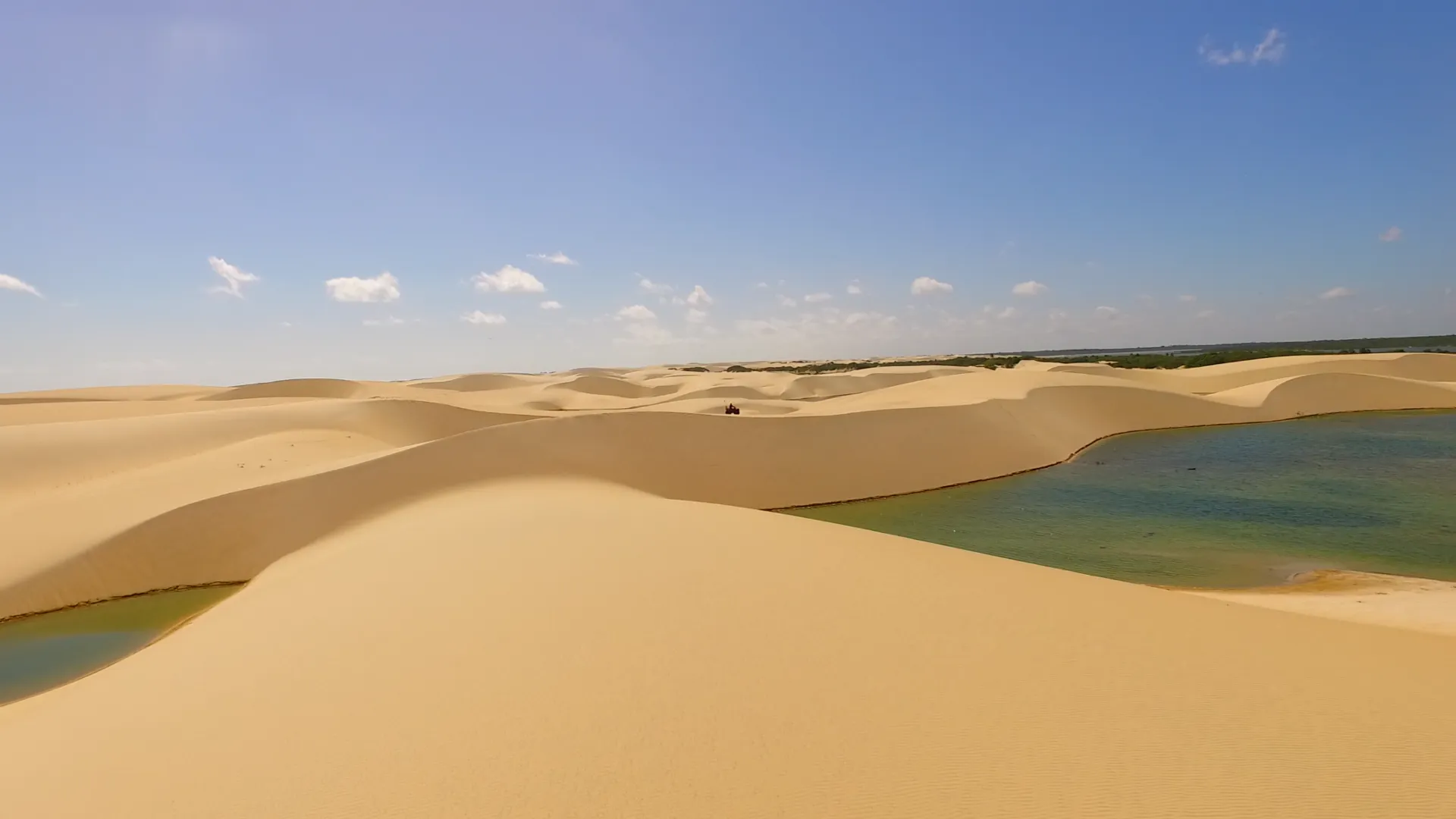 Dunas de areia clara com lagoas de água verde sob um céu azul com poucas nuvens