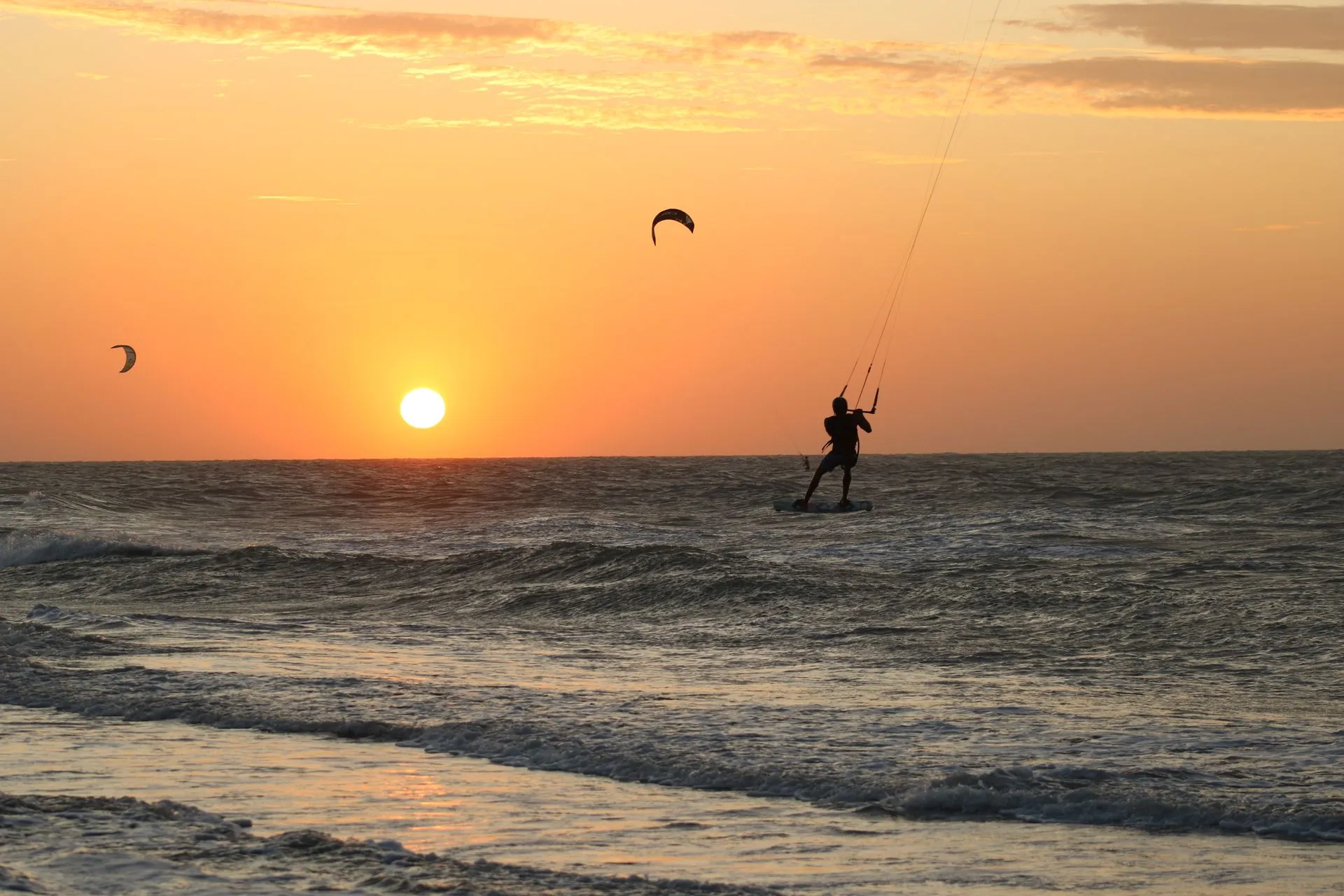 Silhueta de kitesurfista no mar durante o pôr do sol, com dois kites no céu alaranjado