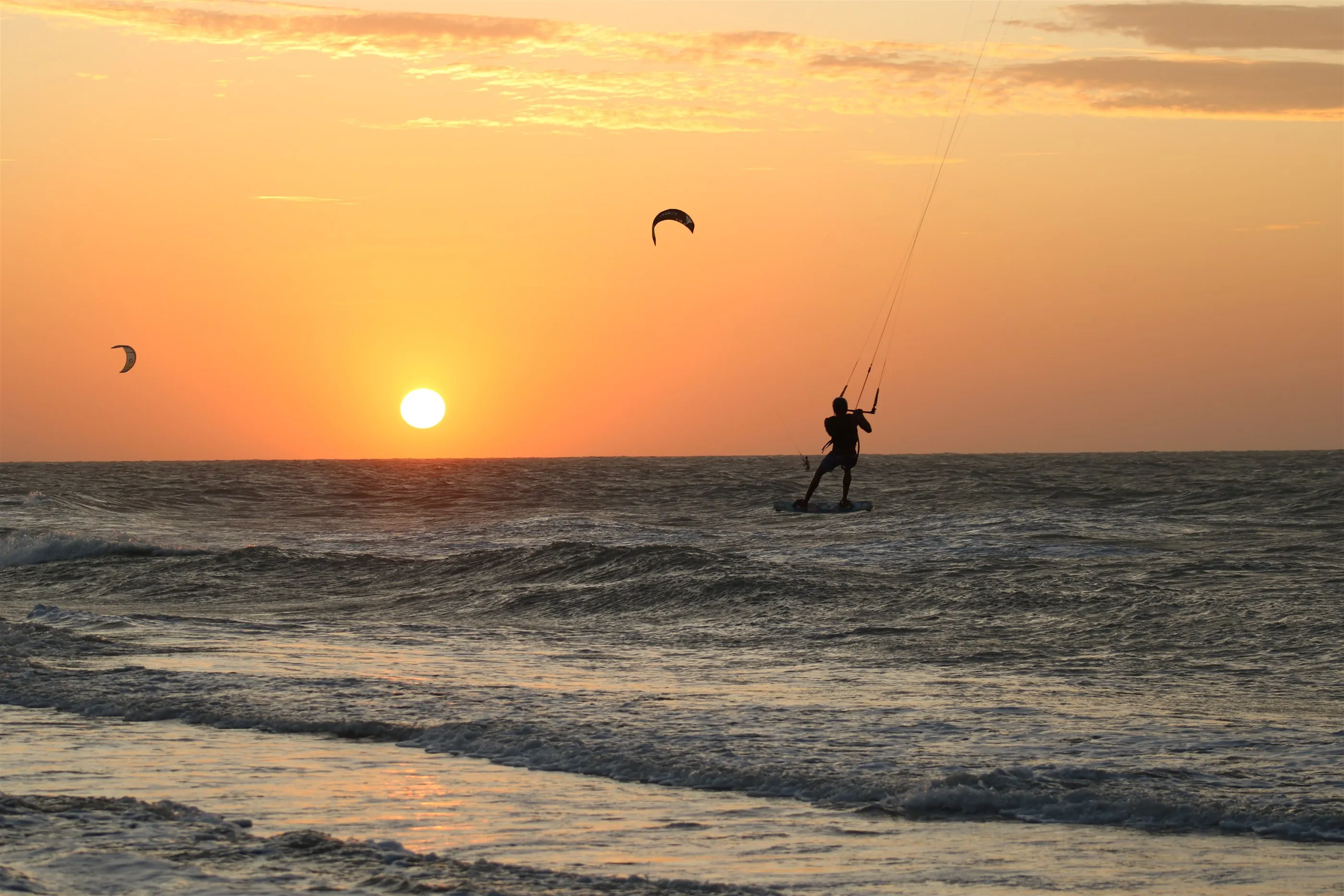 Kitesurfista velejando no mar de Camocim ao pôr do sol, com o sol baixo no horizonte