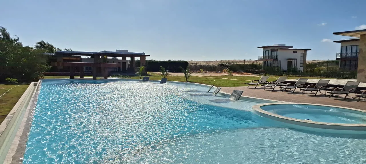 Piscina com hidromassagem ao lado do gramado, com o terraço e as casas do condomínio ao fundo