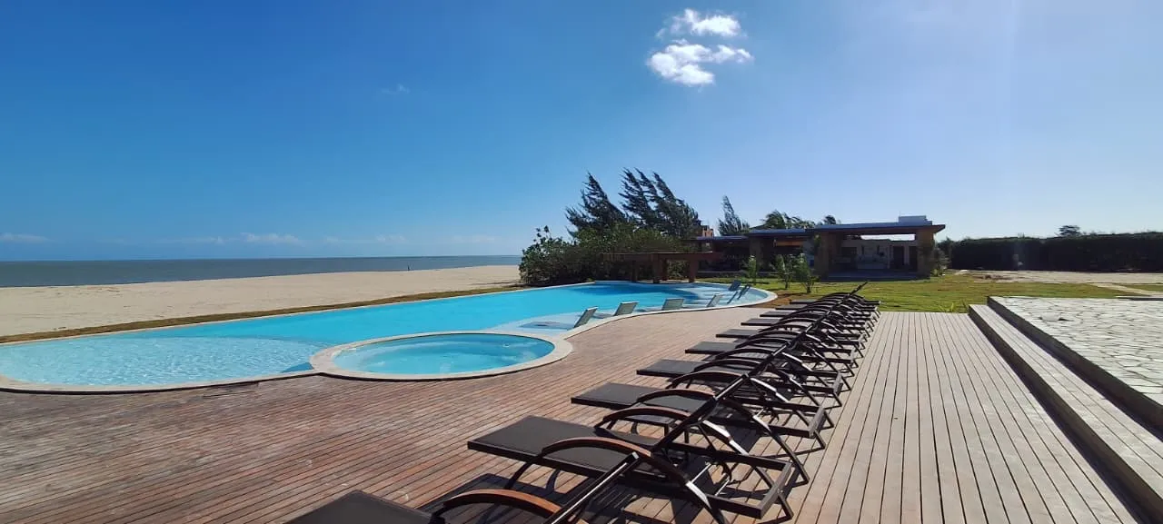 Piscina do condomínio com deck de madeira e espreguiçadeiras, de frente para a faixa de areia e o mar