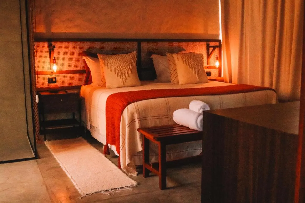 Quarto de casal com cabeceira de madeira, colcha laranja e luminárias de leitura acesas