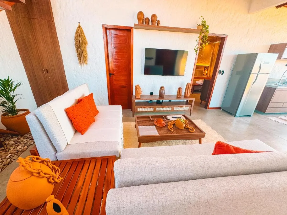 Sala de estar ampla com sofás claros, almofadas laranja e televisão na parede de madeira