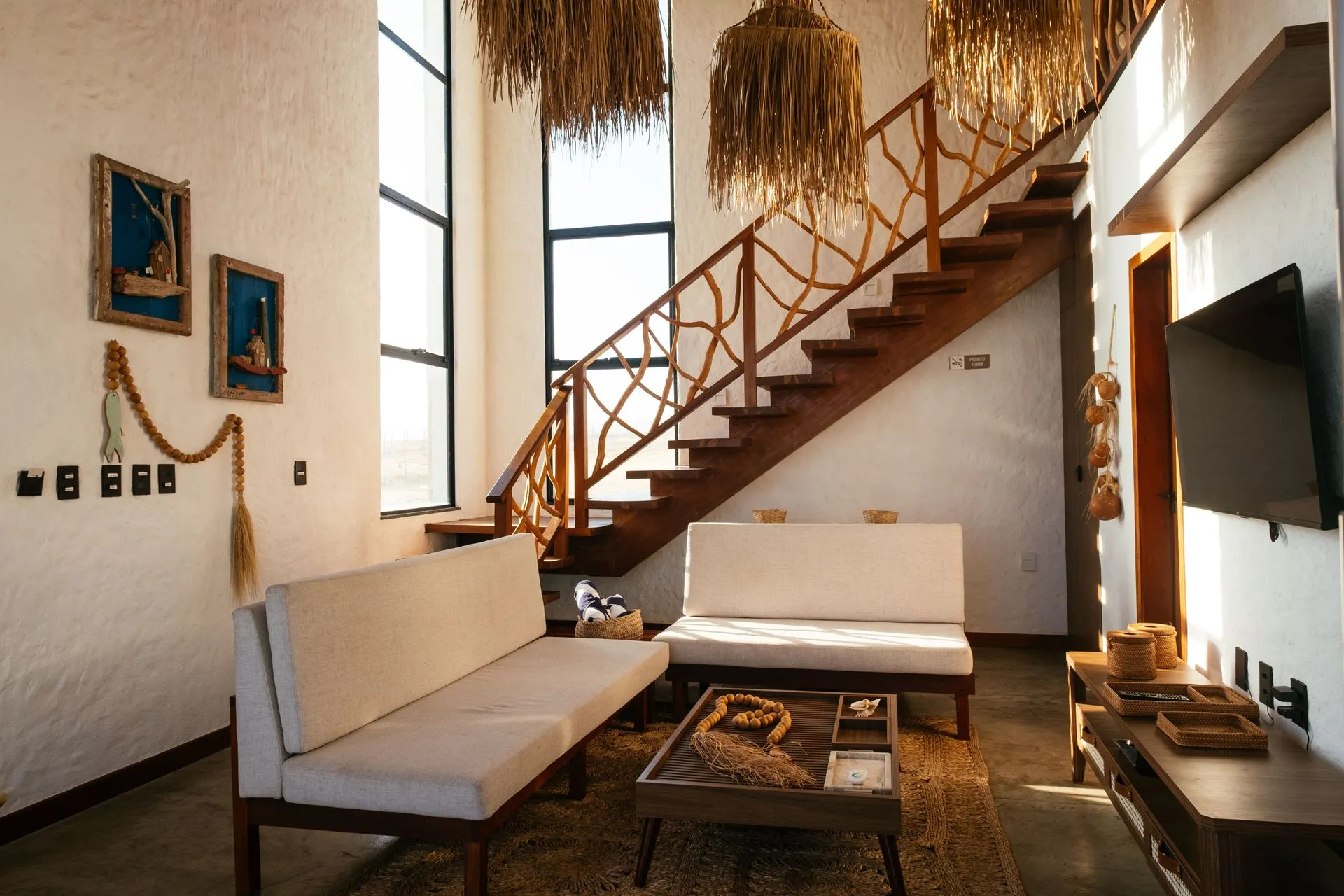 Sala de estar com sofás claros, luminárias de palha e escada de madeira com guarda-corpo de galhos
