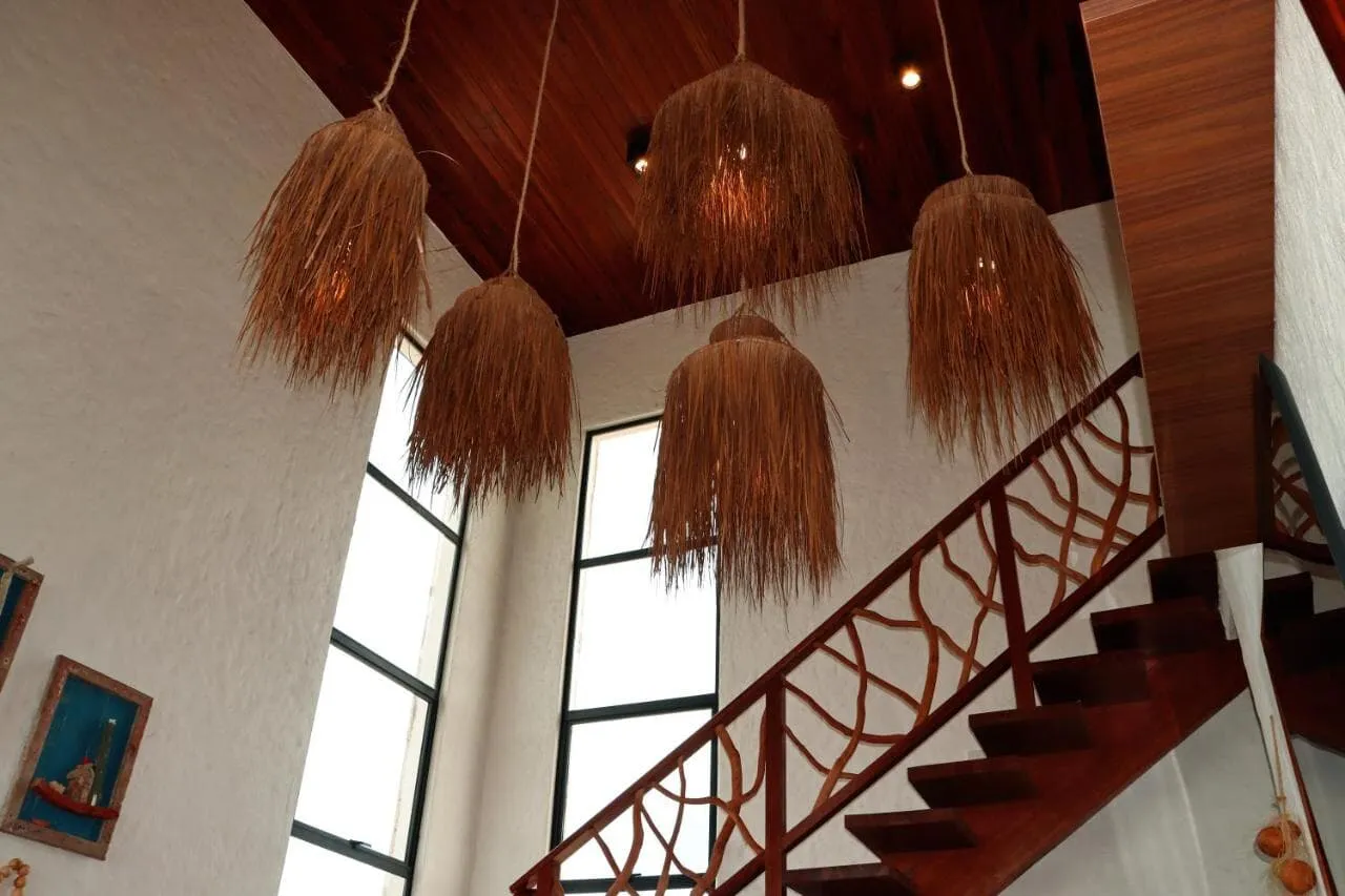 Sala de pé-direito alto com luminárias de palha suspensas e janela que vai do piso ao teto